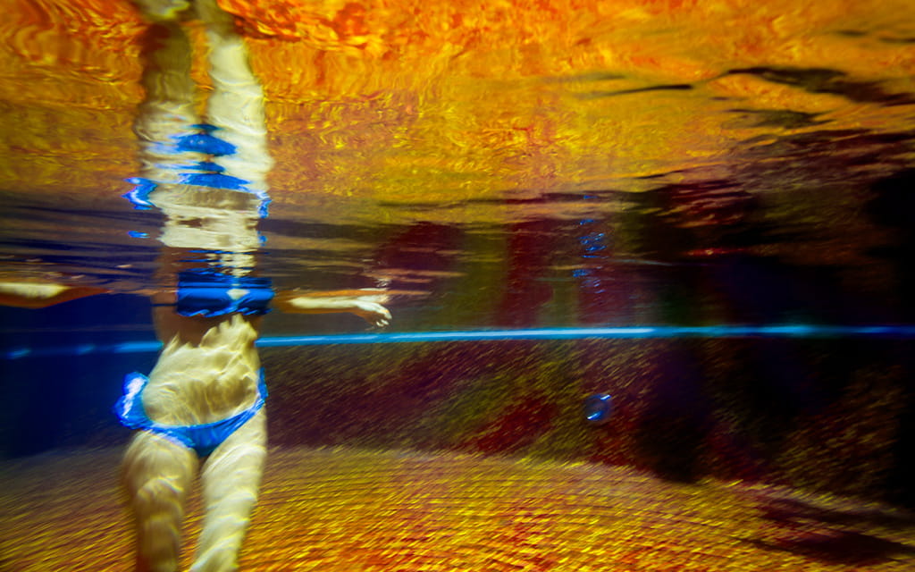 Frau in blauem Bikini läuft im Wasser durch ein beleuchtetes Schwimmbad